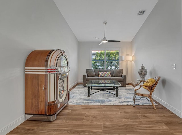 living area with a ceiling fan, visible vents, wood finished floors, baseboards, and lofted ceiling
