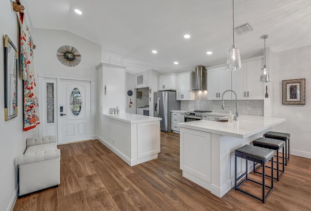 kitchen with visible vents, a peninsula, baseboards, wall chimney range hood, and stainless steel appliances