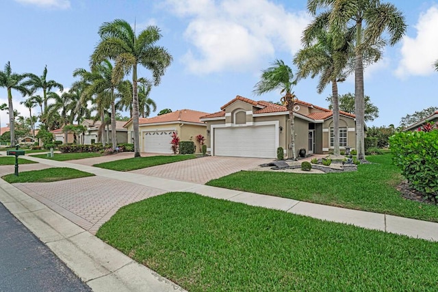 mediterranean / spanish home with a tile roof, a front yard, a garage, decorative driveway, and stucco siding