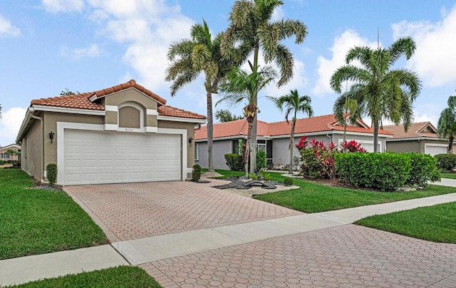 mediterranean / spanish-style house with a garage, stucco siding, a front yard, decorative driveway, and a tiled roof