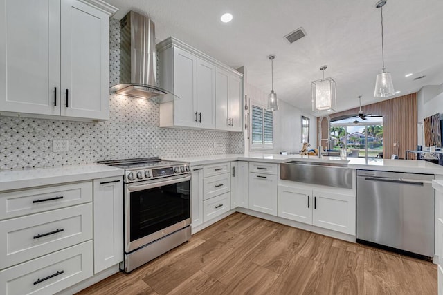 kitchen featuring appliances with stainless steel finishes, a sink, wall chimney exhaust hood, light wood-type flooring, and visible vents