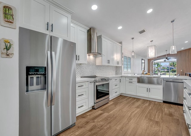 kitchen with appliances with stainless steel finishes, light wood finished floors, light countertops, wall chimney exhaust hood, and visible vents