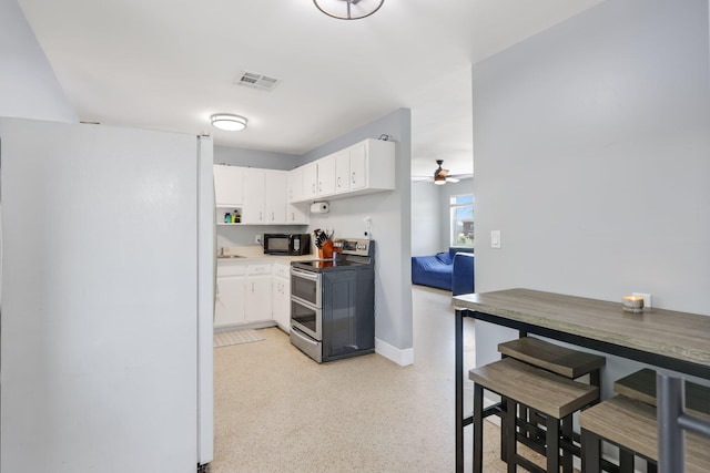 2136 W Carrol Cir, West Palm Beach, FL 33415 - kitchen with stainless steel electric range oven, black microwave, freestanding refrigerator, ceiling fan, and white cabinetry