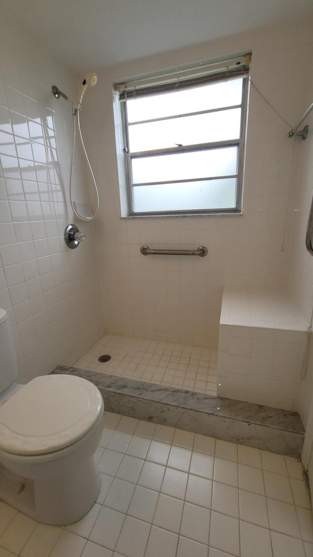 bathroom featuring toilet, tile patterned flooring, a tile shower, and healthy amount of natural light