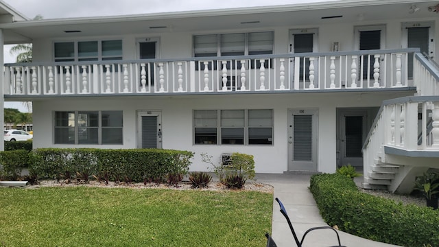 view of front of house with stucco siding, a balcony, and a front lawn