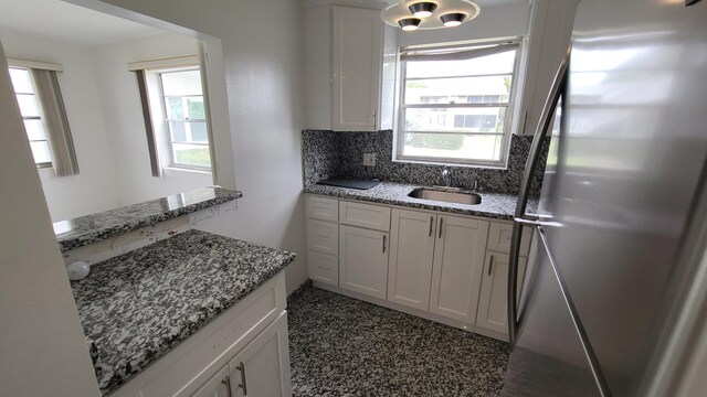 kitchen with freestanding refrigerator, a sink, backsplash, white cabinetry, and healthy amount of natural light