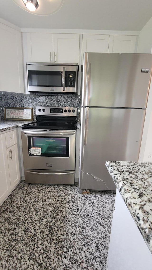 kitchen featuring stainless steel appliances, white cabinetry, and light stone countertops
