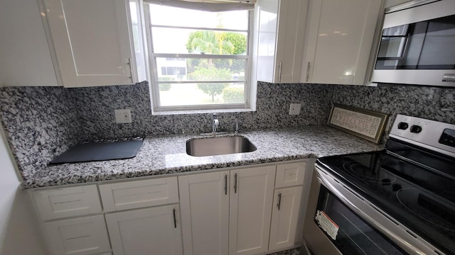 kitchen with appliances with stainless steel finishes, a sink, white cabinetry, and tasteful backsplash