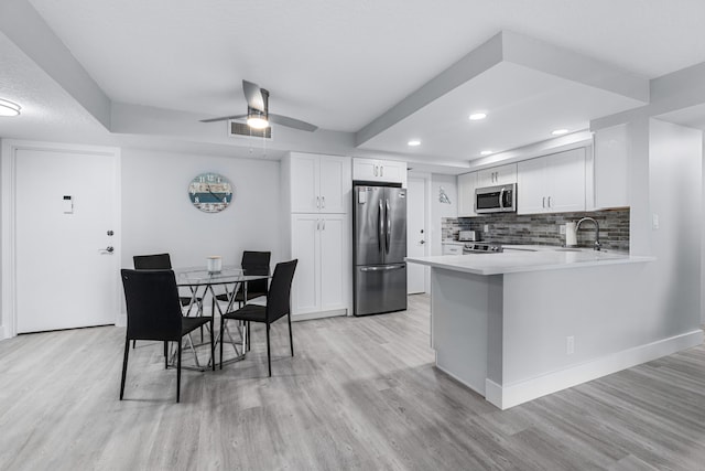 kitchen featuring stainless steel appliances, a peninsula, light wood-style flooring, and tasteful backsplash