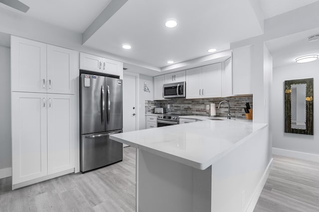 kitchen featuring appliances with stainless steel finishes, a sink, light countertops, baseboards, and light wood-type flooring