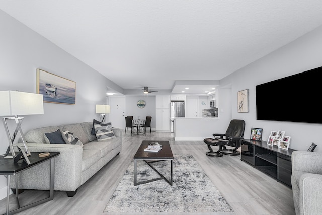 living room featuring baseboards, a ceiling fan, and light wood finished floors