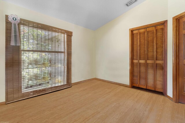 unfurnished bedroom with baseboards, visible vents, wood finished floors, and vaulted ceiling