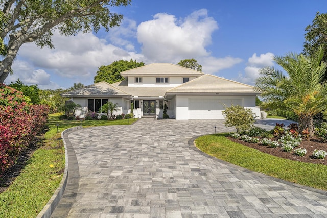 prairie-style home featuring a garage, stucco siding, decorative driveway, and french doors