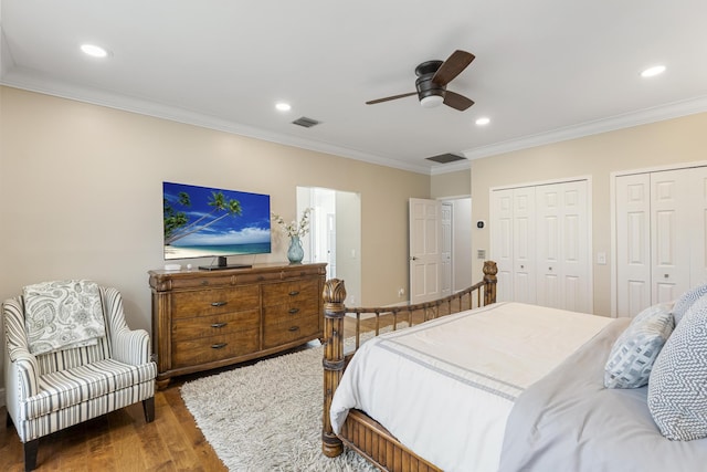 bedroom with crown molding, two closets, recessed lighting, wood finished floors, and visible vents