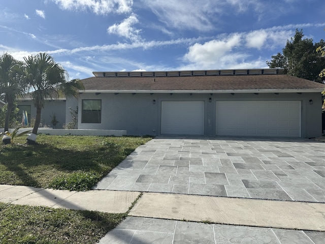 view of front of property with decorative driveway, an attached garage, a front lawn, and stucco siding