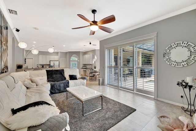 living area with a ceiling fan, visible vents, baseboards, ornamental molding, and light tile patterned flooring