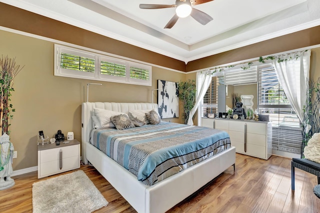 bedroom featuring a ceiling fan, baseboards, light wood-style flooring, and a raised ceiling