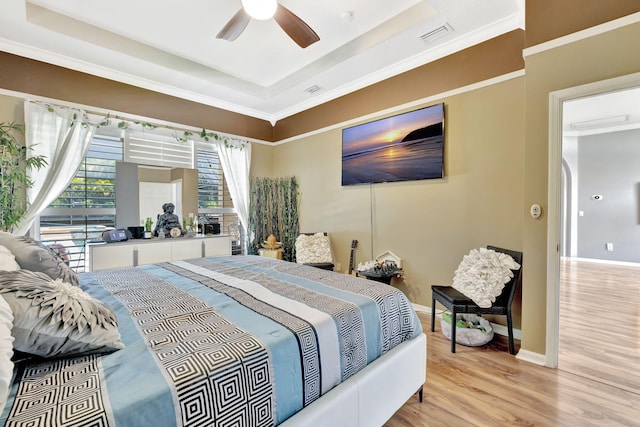 bedroom with light wood-style floors, baseboards, crown molding, and a tray ceiling