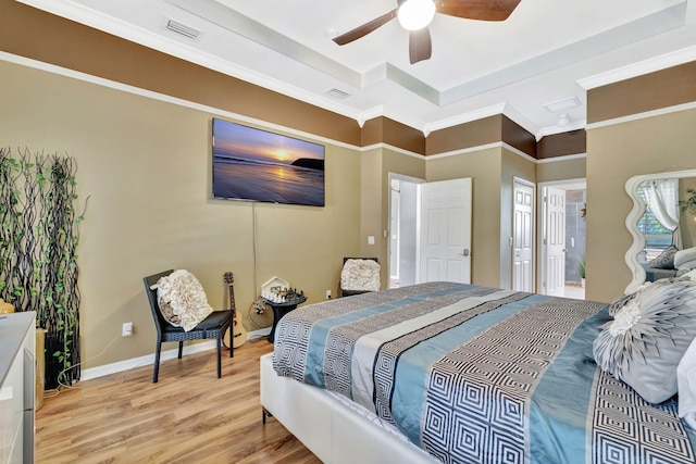 bedroom with light wood-style floors, a raised ceiling, crown molding, and visible vents