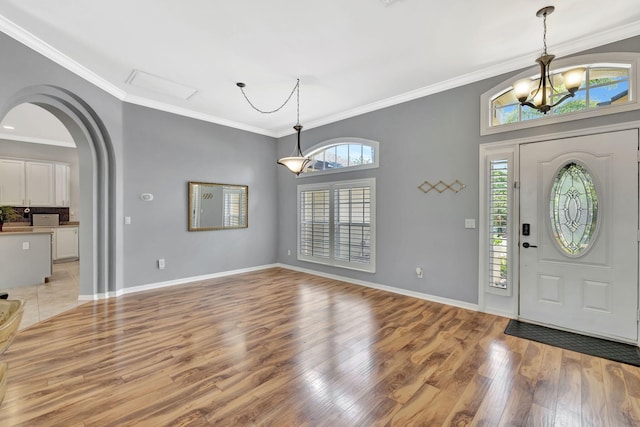 entryway with crown molding, arched walkways, light wood-type flooring, baseboards, and an inviting chandelier