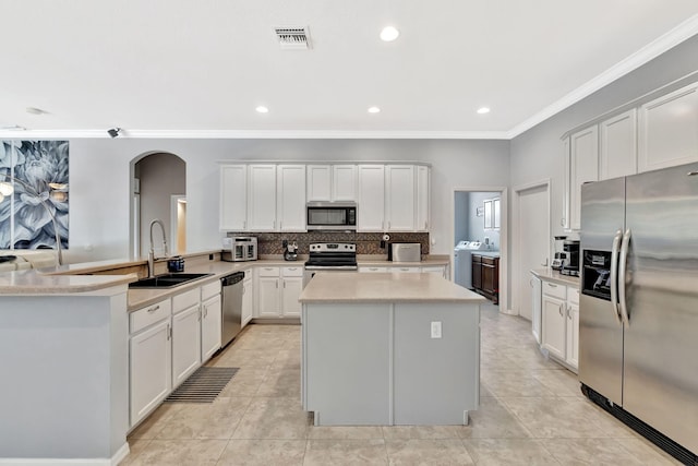 kitchen featuring a sink, arched walkways, stainless steel appliances, a kitchen island, and washing machine and dryer