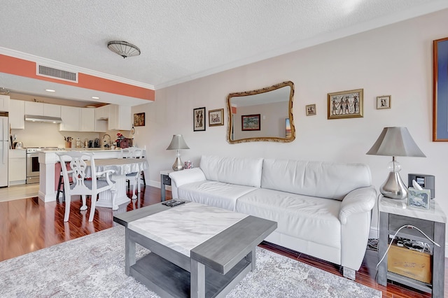 living room featuring a textured ceiling, visible vents, ornamental molding, and wood finished floors