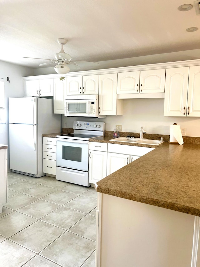 kitchen with white cabinets, dark countertops, a sink, white appliances, and light tile patterned floors