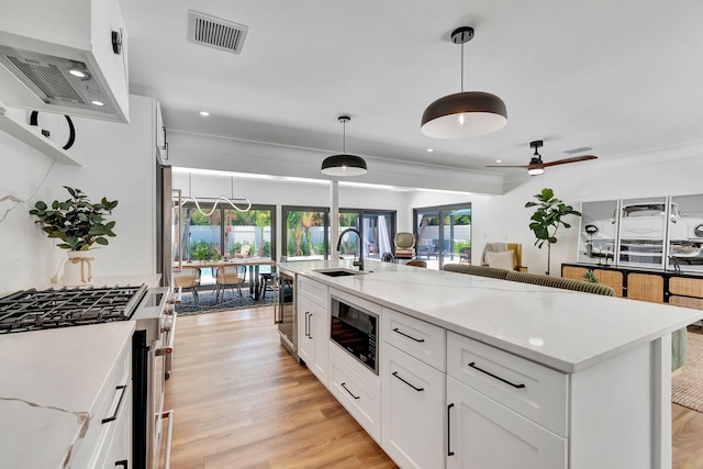 kitchen with wall chimney range hood, visible vents, black microwave, gas stove, and a sink
