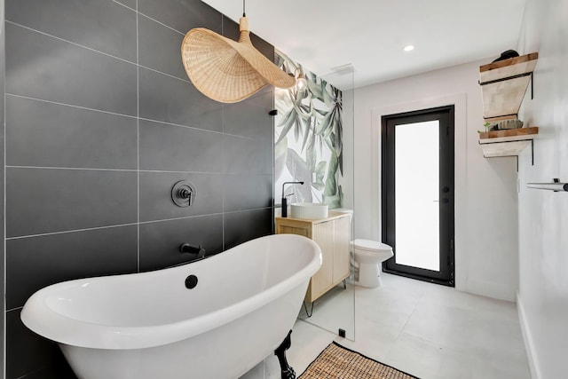 bathroom featuring a freestanding bath, tile walls, vanity, tile patterned floors, and toilet