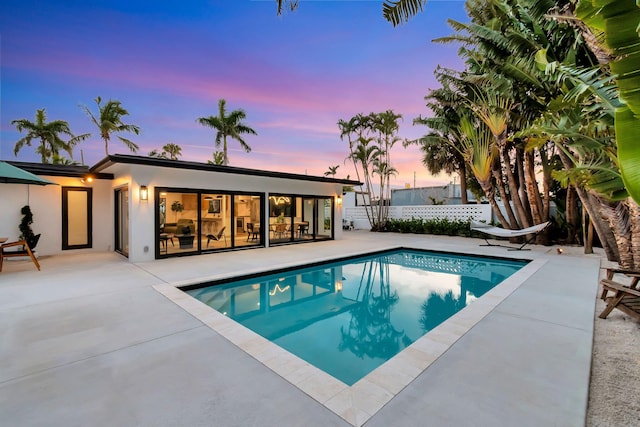 pool at dusk featuring fence, a fenced in pool, and a patio area