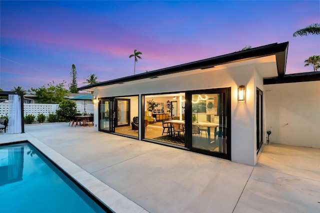 back of property at dusk featuring fence, a fenced in pool, stucco siding, and a patio area