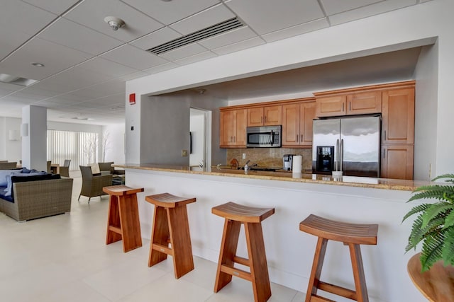 2800 S Ocean Blvd Unit 23C, Boca Raton, FL 33432 - kitchen with decorative backsplash, a kitchen bar, visible vents, brown cabinets, and stainless steel appliances
