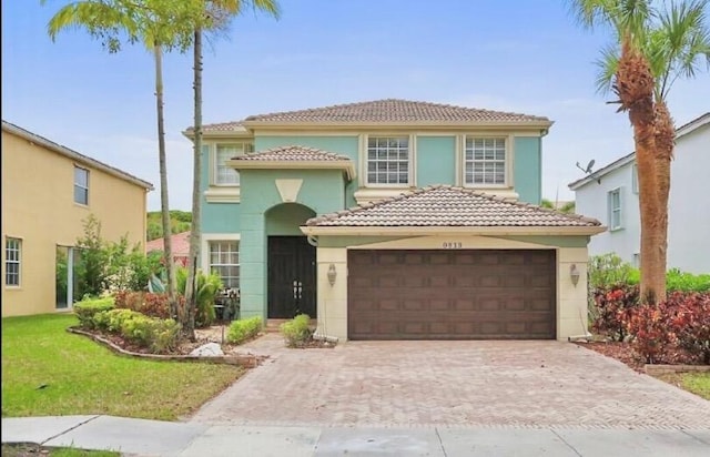 mediterranean / spanish home featuring an attached garage, a tile roof, stucco siding, a front yard, and decorative driveway