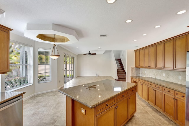 kitchen featuring visible vents, decorative backsplash, brown cabinetry, stainless steel dishwasher, and light stone counters