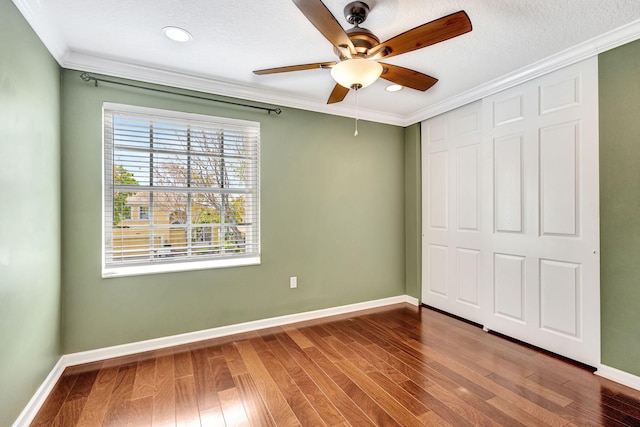 unfurnished bedroom with ceiling fan, baseboards, wood finished floors, ornamental molding, and a closet