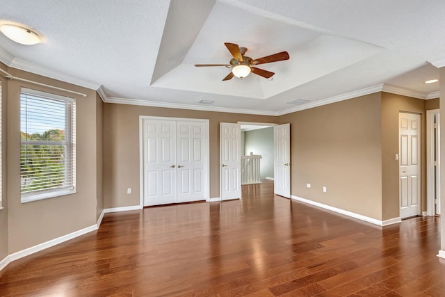 unfurnished bedroom with crown molding, ceiling fan, a raised ceiling, baseboards, and wood finished floors