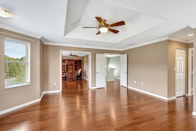unfurnished living room featuring a ceiling fan, baseboards, wood finished floors, a tray ceiling, and ornamental molding