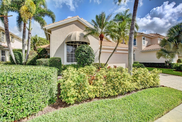 view of front of house with an attached garage, stucco siding, a tile roof, and driveway