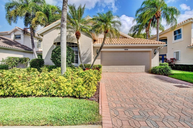 mediterranean / spanish house with stucco siding, a garage, a tiled roof, and driveway