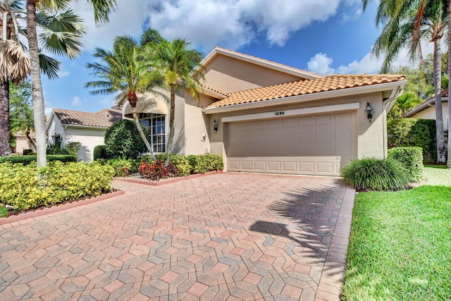 mediterranean / spanish house featuring an attached garage, stucco siding, a tile roof, and decorative driveway