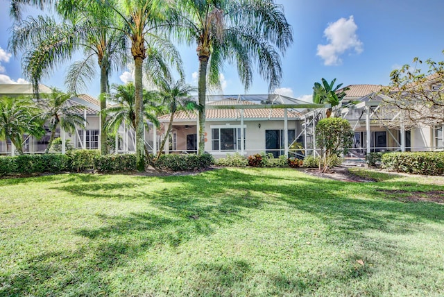 view of front of home featuring glass enclosure, a tile roof, stucco siding, a front yard, and ceiling fan