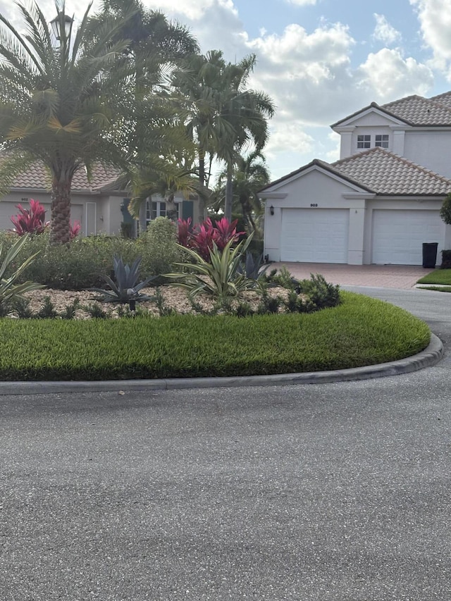 view of front facade with driveway, stucco siding, a tile roof, and a garage