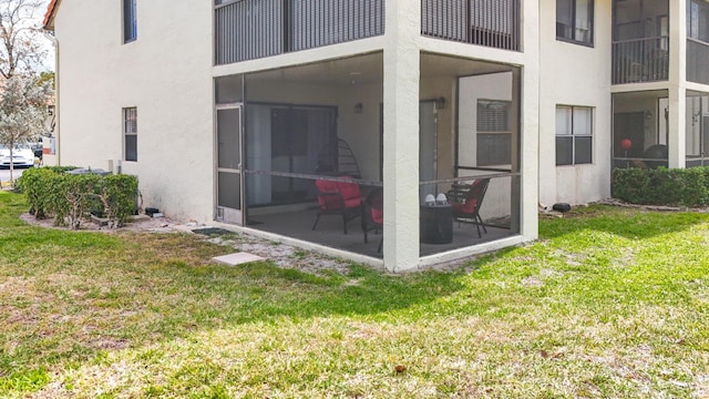 back of property featuring a yard, a sunroom, and stucco siding