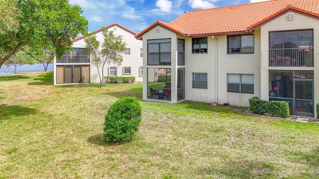 back of property featuring a lawn, stucco siding, a water view, and a tile roof