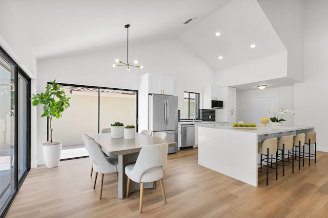 2795 Hawthorne Ln, West Palm Beach, FL 33409 - kitchen with stainless steel appliances, white cabinetry, high vaulted ceiling, light wood-style flooring, and a breakfast bar area