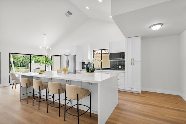 2795 Hawthorne Ln, West Palm Beach, FL 33409 - kitchen featuring black microwave, freestanding refrigerator, white cabinetry, a breakfast bar area, and high vaulted ceiling