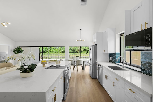 2795 Hawthorne Ln, West Palm Beach, FL 33409 - kitchen with stainless steel appliances, a sink, a chandelier, white cabinets, and high vaulted ceiling