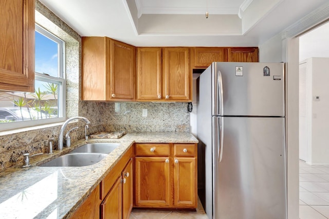 kitchen featuring a sink, a raised ceiling, freestanding refrigerator, light tile patterned floors, and tasteful backsplash