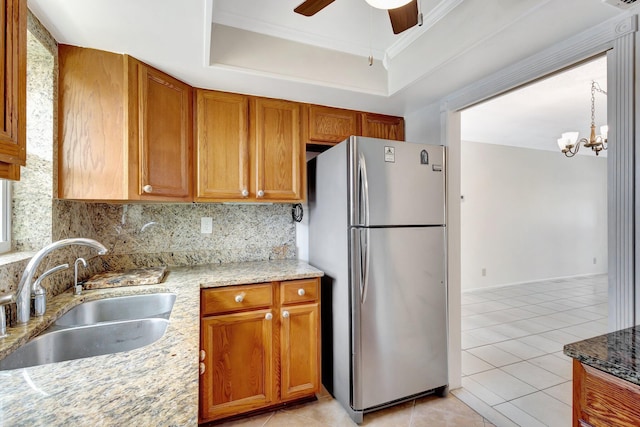 kitchen featuring freestanding refrigerator, tasteful backsplash, a sink, ceiling fan with notable chandelier, and light tile patterned floors