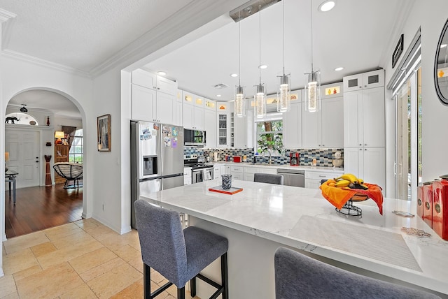 4474 Thornwood Cir, Palm Beach Gardens, FL 33418 - kitchen featuring appliances with stainless steel finishes, a kitchen breakfast bar, tasteful backsplash, ornamental molding, and arched walkways